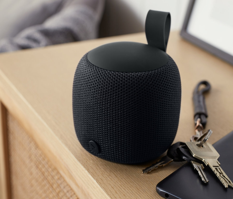 Anthrazitfarbener Design-Bluetooth®-Lautsprecher S auf einem Holztisch neben einem Handy und Schlüsseln.