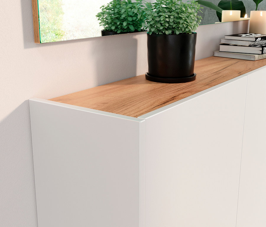 Detailaufnahme eines weißen Mehrzweckschranks "Libbiano" mit Holzplatte, auf der eine Topfpflanze, Bücher und Kerzen stehen.
