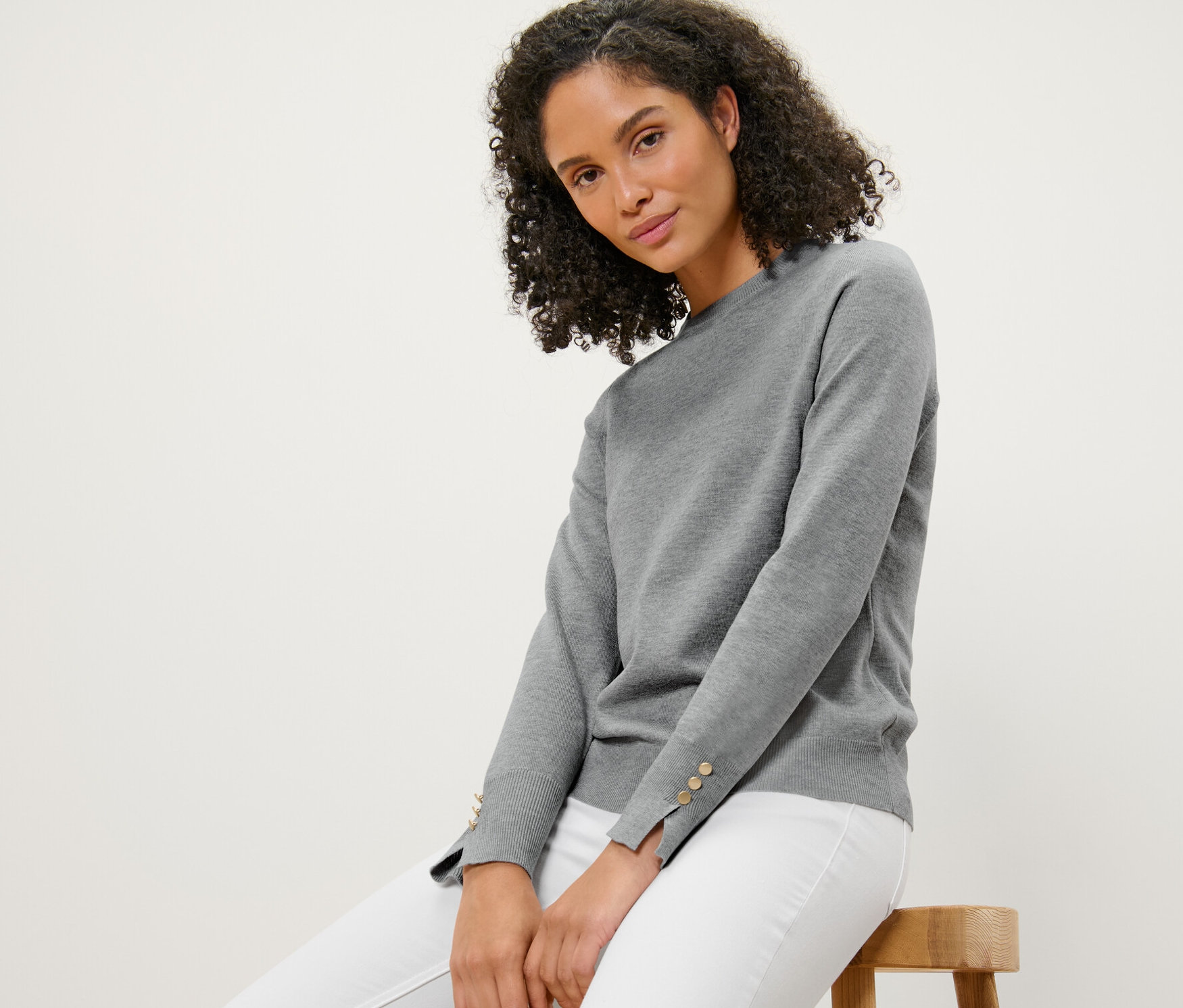 Frau sitzt auf einem Hocker und trägt einen grau melierten Feinstrickpullover.
