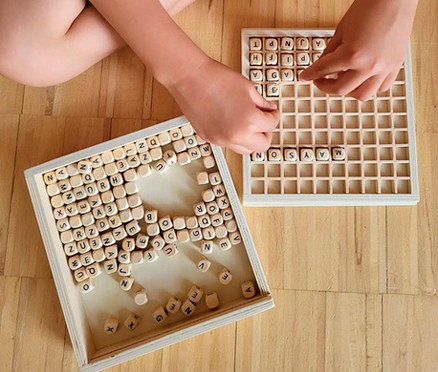 Kind sitzt am Boden und spielt mit small foot Wörter legen »Educate«.