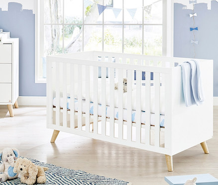 Ein weißes Pinolino Babybett »Move« steht in einem Kinderzimmer mit blauen Akzenten.