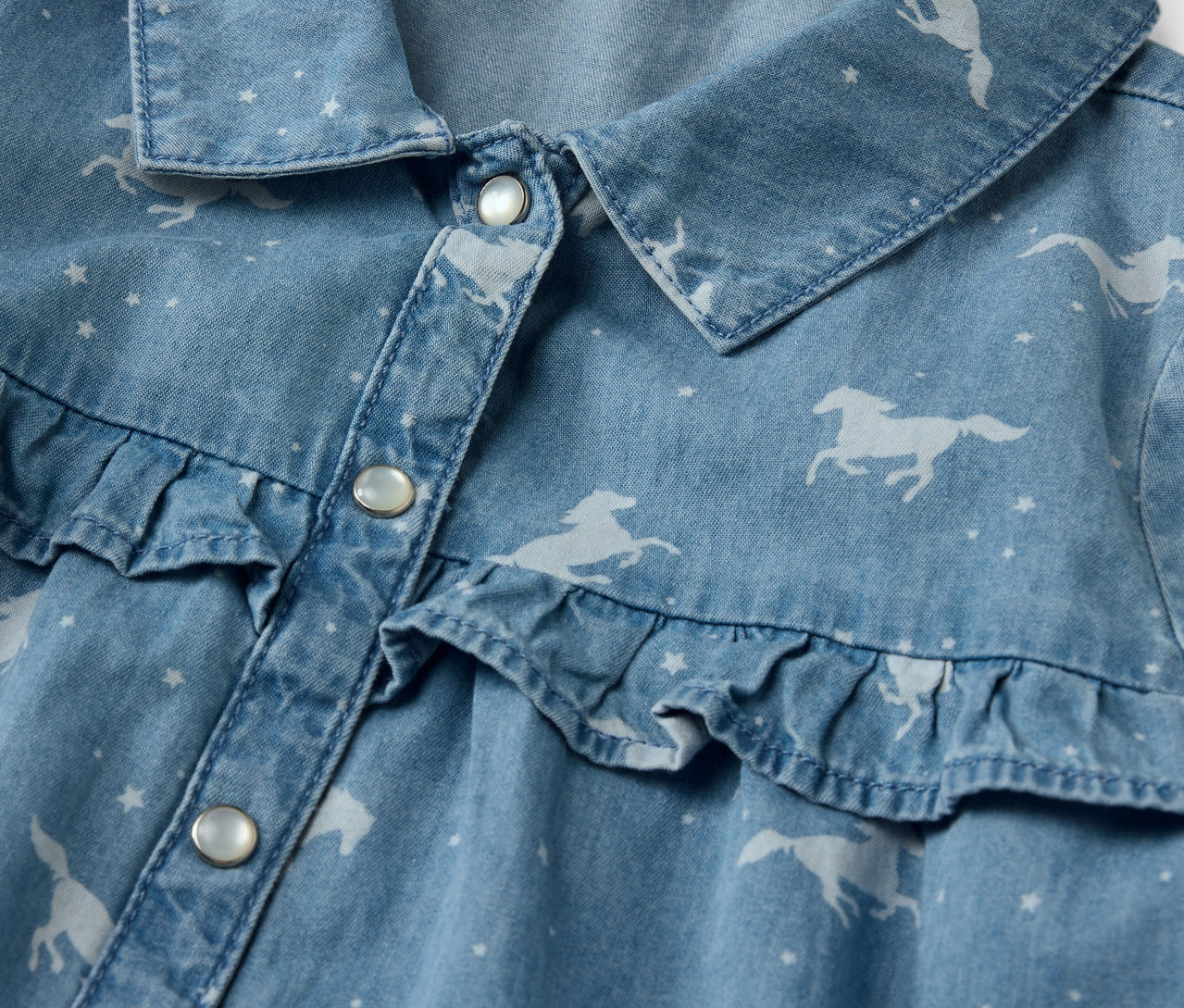 Detailaufnahme eines Kinder-Jeanskleids mit Pferdeaufdruck und Rüschen.
