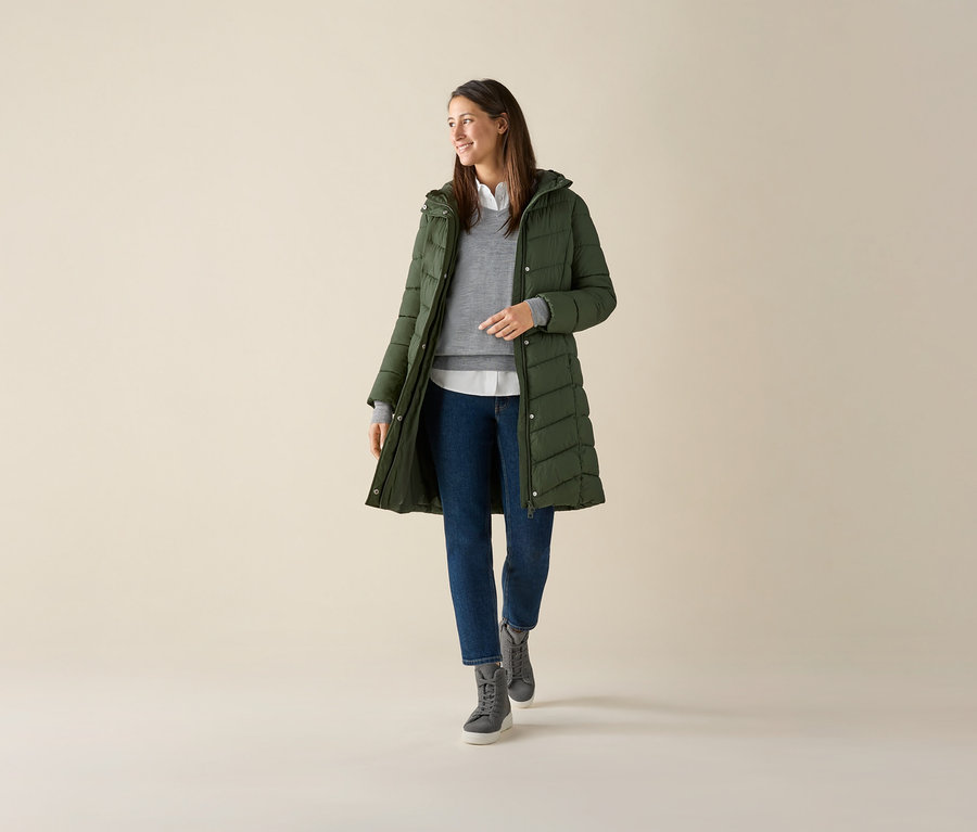 Frau trägt grauen Merino-Feinstrickpullover, grüne Jacke und Jeans.