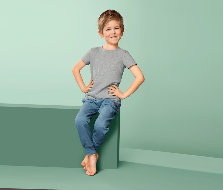 Ein Junge sitzt auf einem grünen Block und trägt 2 Unterhemden.