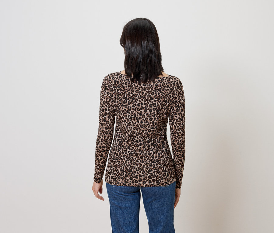 Frau steht mit dem Rücken und trägt ein braunes, langärmeliges Oberteil mit Tiermuster und blaue Jeans.