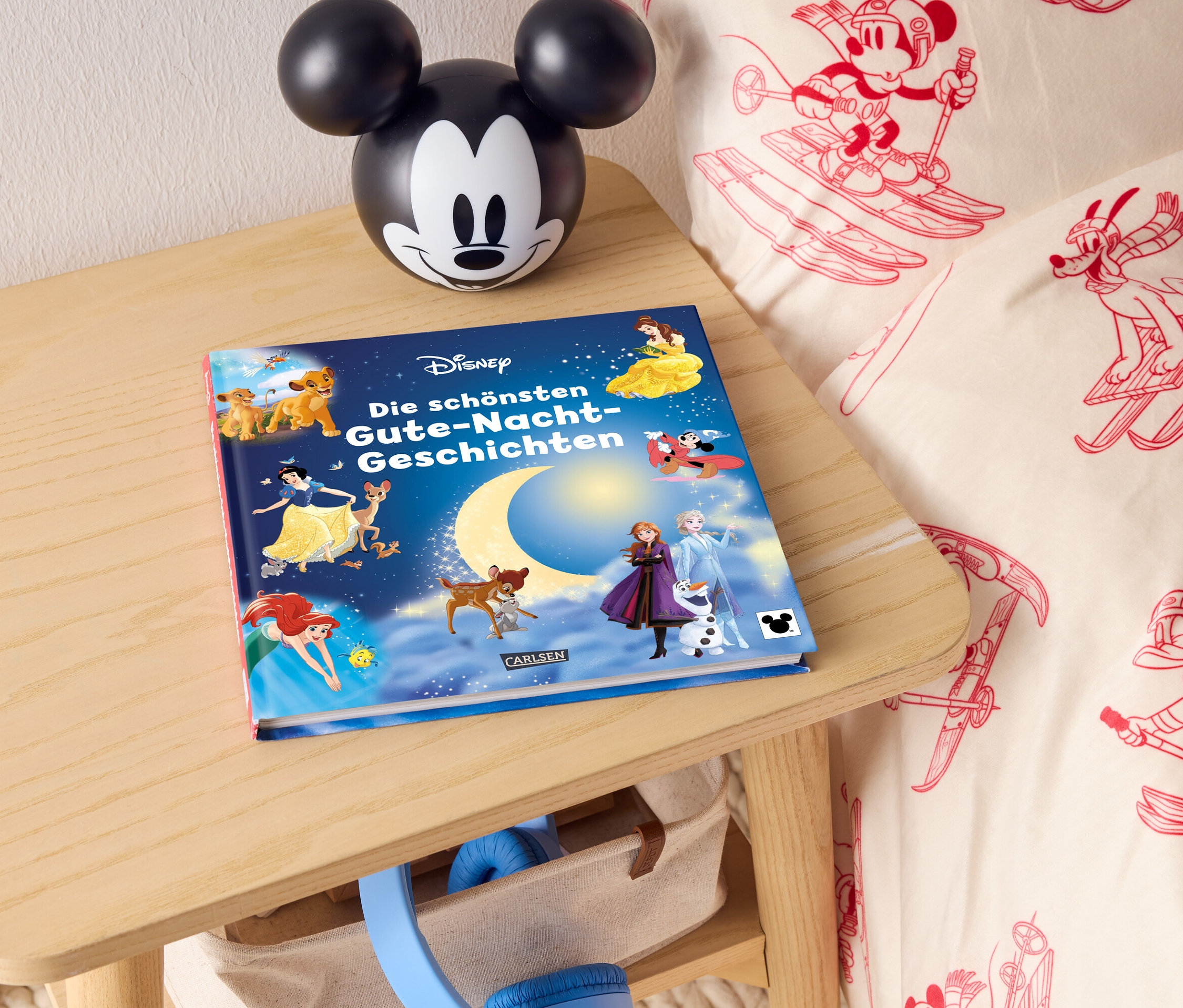 Auf einem Nachttisch liegen ein Disney Gute-Nacht-Geschichtenbuch und eine Mickey-Mouse-Lampe.