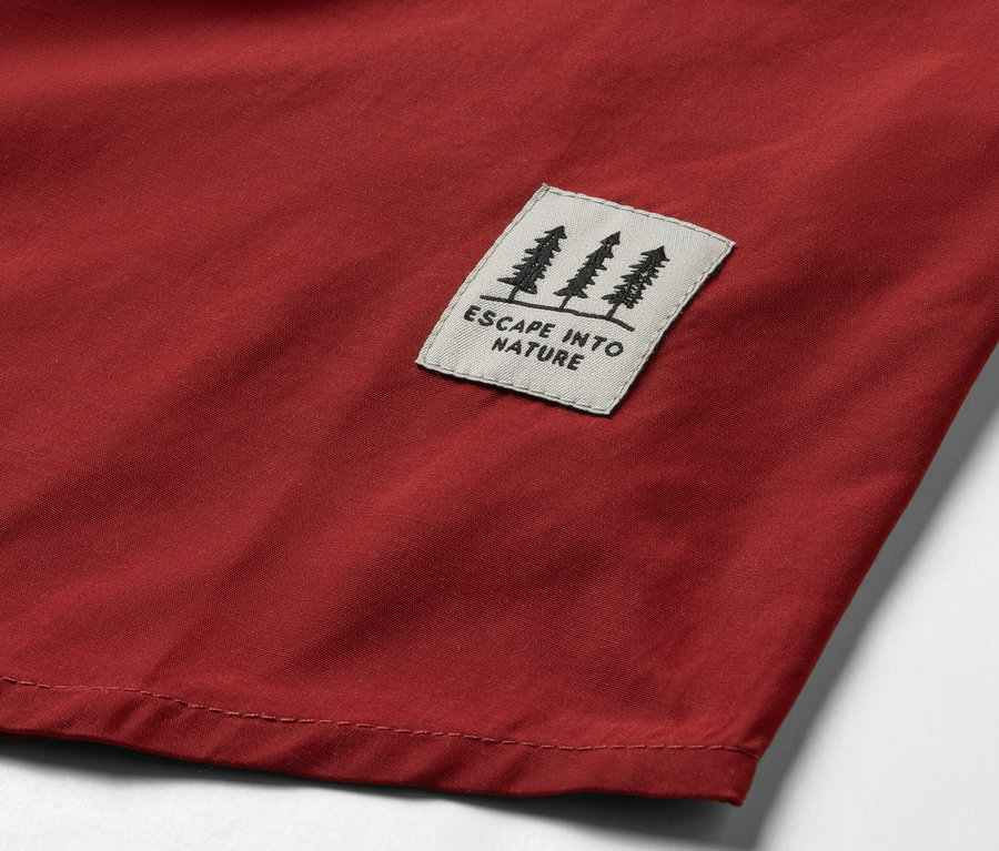 Detail einer roten Outdoorbluse mit einem Aufnäher mit einem Baummotiv und dem Schriftzug „ESCAPE INTO NATURE“.