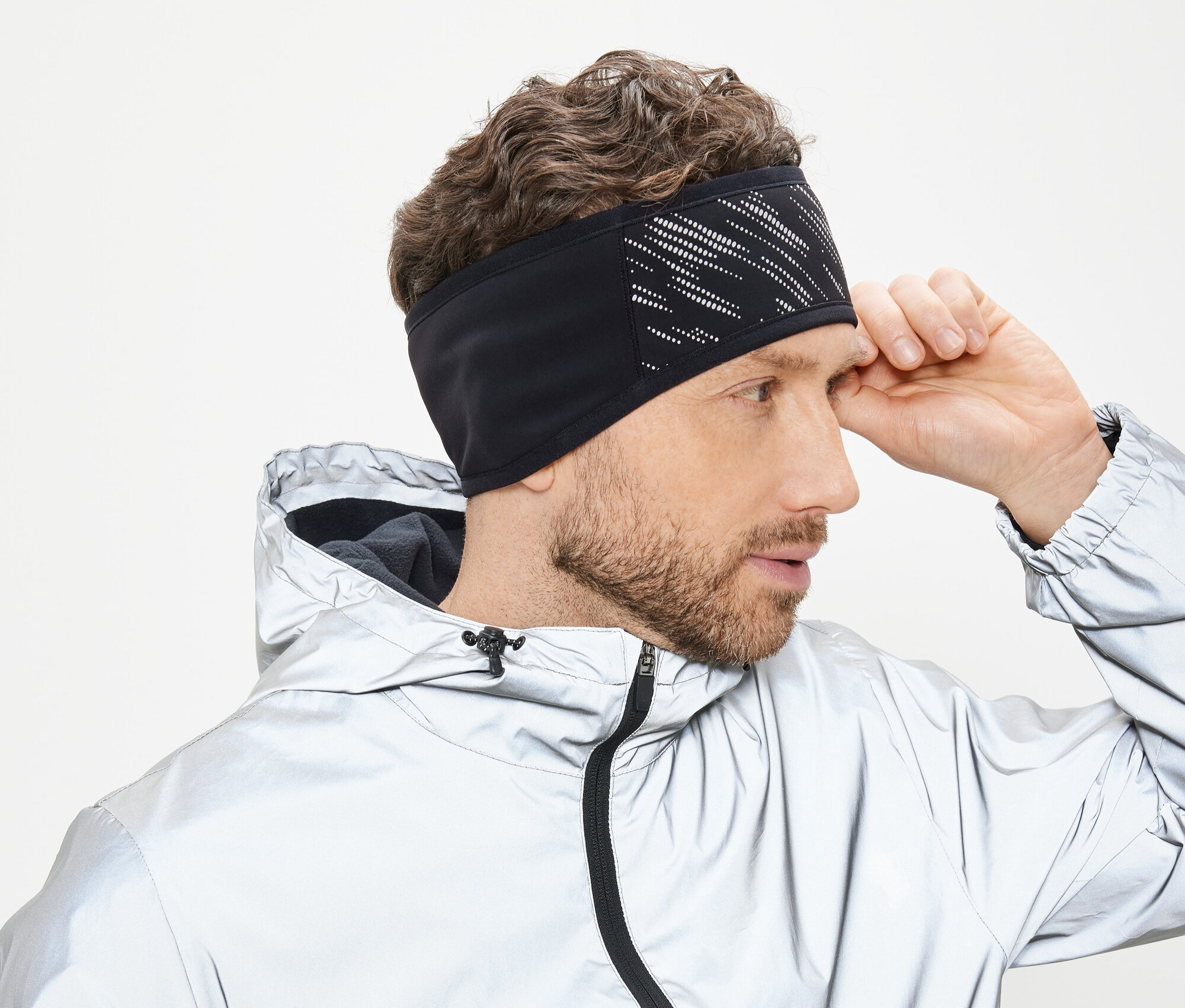 Mann richtet schwarzes Stirnband mit weißem Muster. Er trägt eine silberne Jacke mit Kapuze.