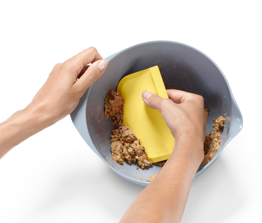 Ein paar Hände mischen Teig in einer Schüssel mit einem gelben Spatel.