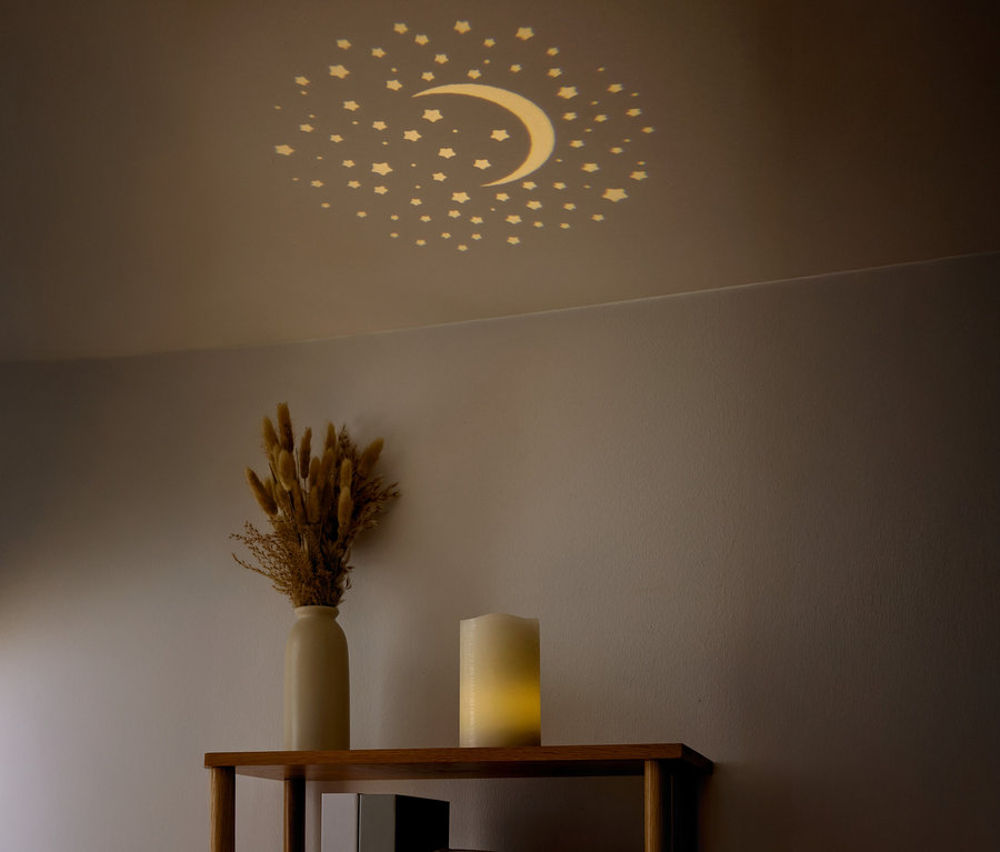 An der Decke sind Sterne und ein Halbmond sichtbar. Auf einem Regal stehen eine Vase mit getrockneten Blumen und eine Kerze.