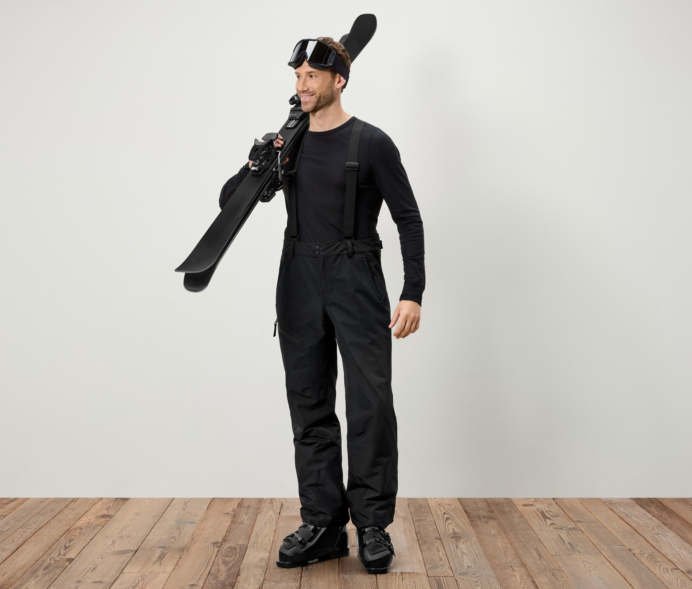 Mann in schwarzer Skikleidung trägt Ski über der Schulter.