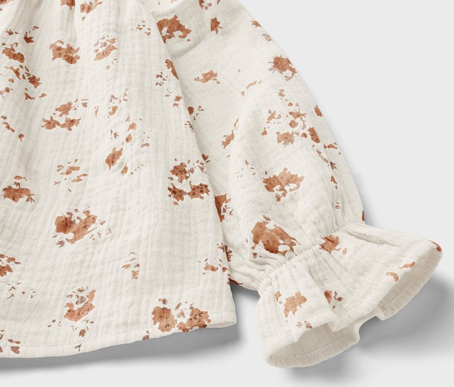 Detailaufnahme einer Kinder-Musselin-Bluse mit braunem Blumenmuster und Rüschen am Ärmel.