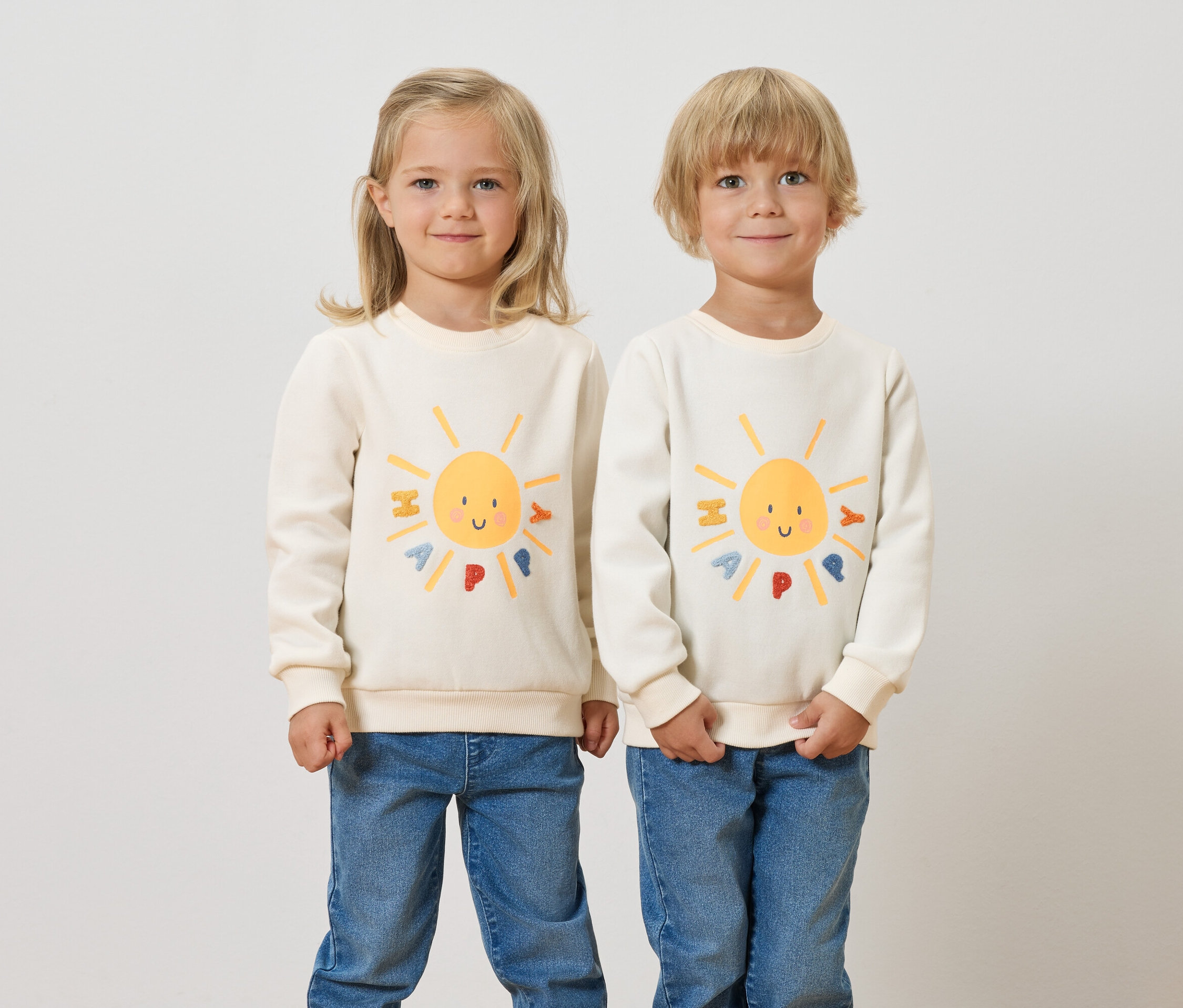 Zwei Kinder stehen nebeneinander und tragen Kinder-Sweatshirts mit angerauter Innenseite und einem Sonne-Motiv.