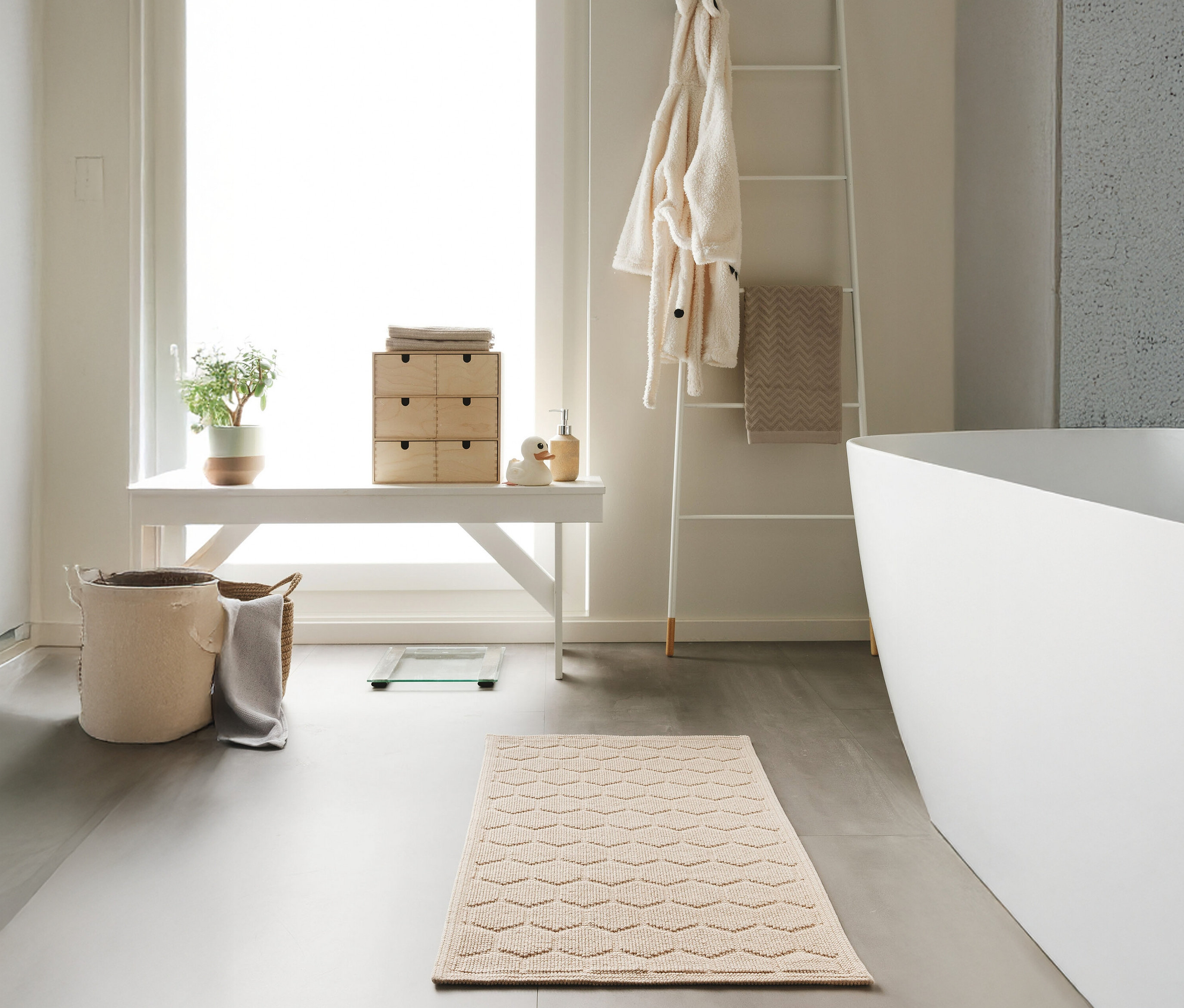 Ein Badezimmer mit einer beigen benuta Badematte »Jojo« mit Rautenmuster, Größe 50 x 80 cm, vor einer weißen Badewanne.