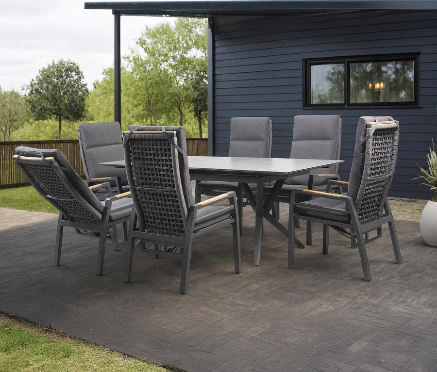 Grauer Gartentisch mit sechs Stühlen auf einer Terrasse vor einem Haus.