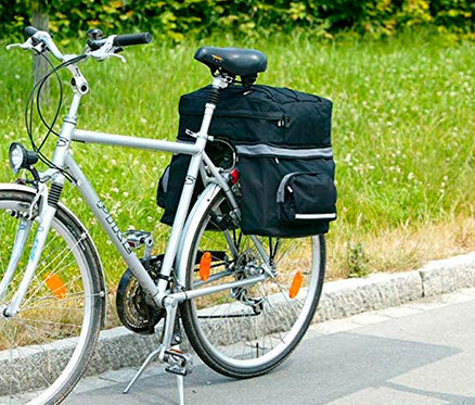 Ein silbernes Fahrrad mit einer schwarzen FISCHER Gepäckträgertasche auf dem Gepäckträger steht auf einem Bürgersteig.