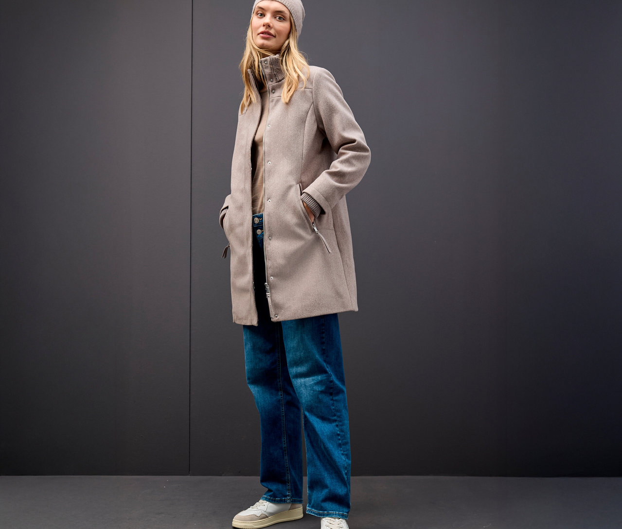 Frau mit beiger Mütze und Street One Kurzmantel vor grauem Hintergrund.