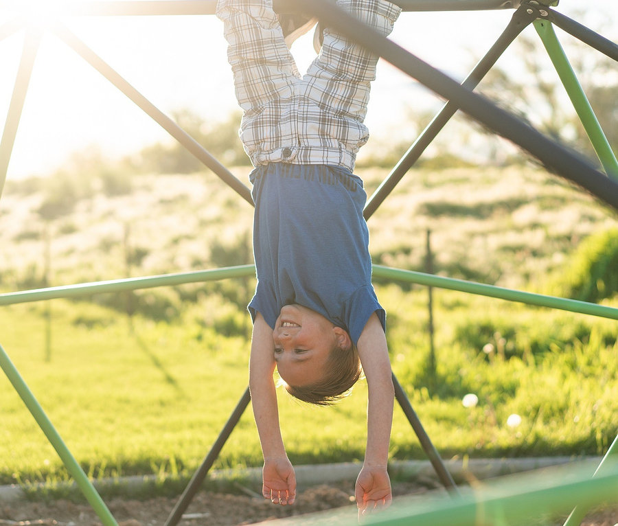 Junge hängt kopfüber an großem LIFETIME-Klettergerüst »Geodome«.
