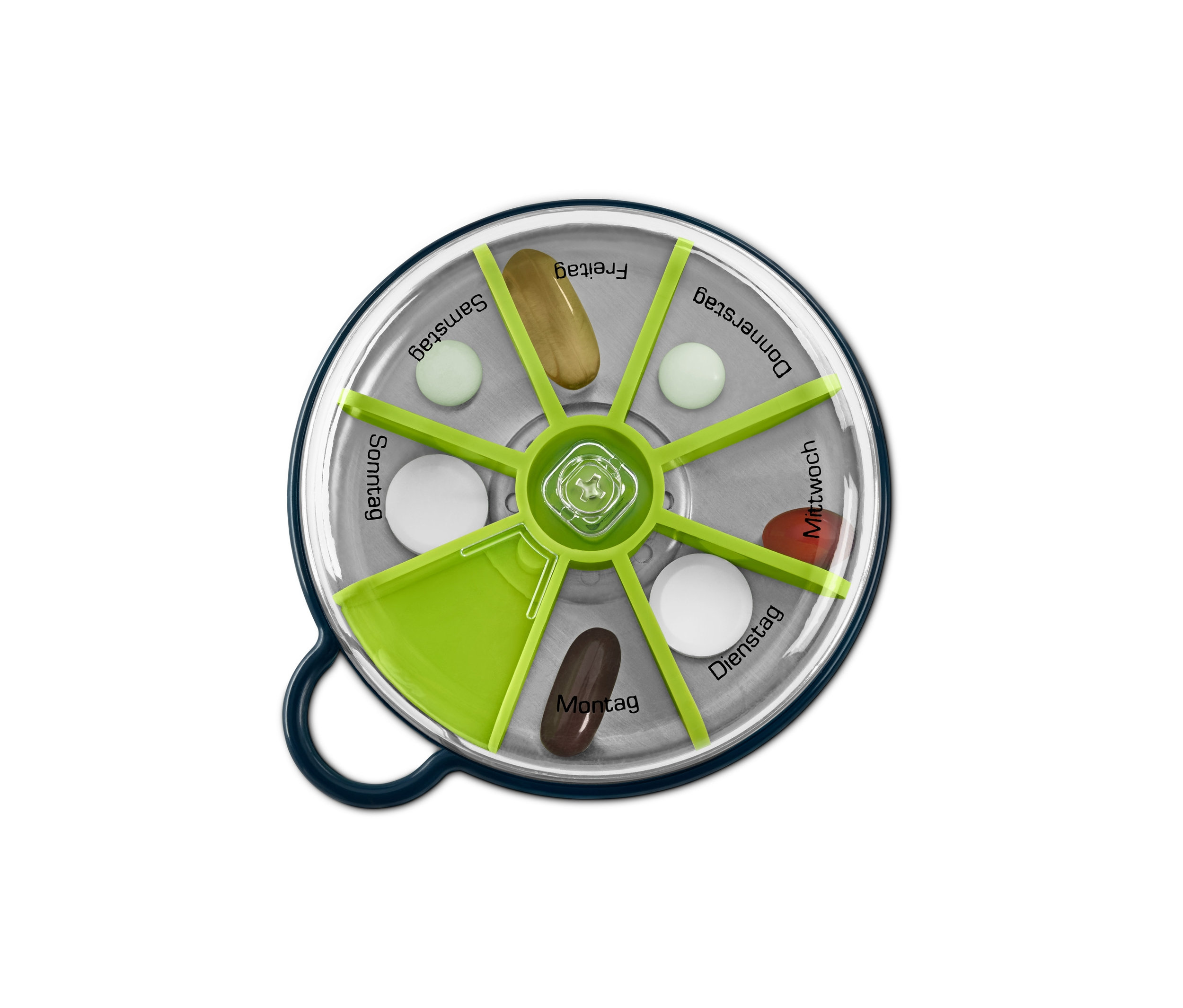 Draufsicht auf eine runde, durchsichtige, grün-silberne Pillendose mit verschiedenen Pillen in Fächern, die mit Wochentagen beschriftet sind.
