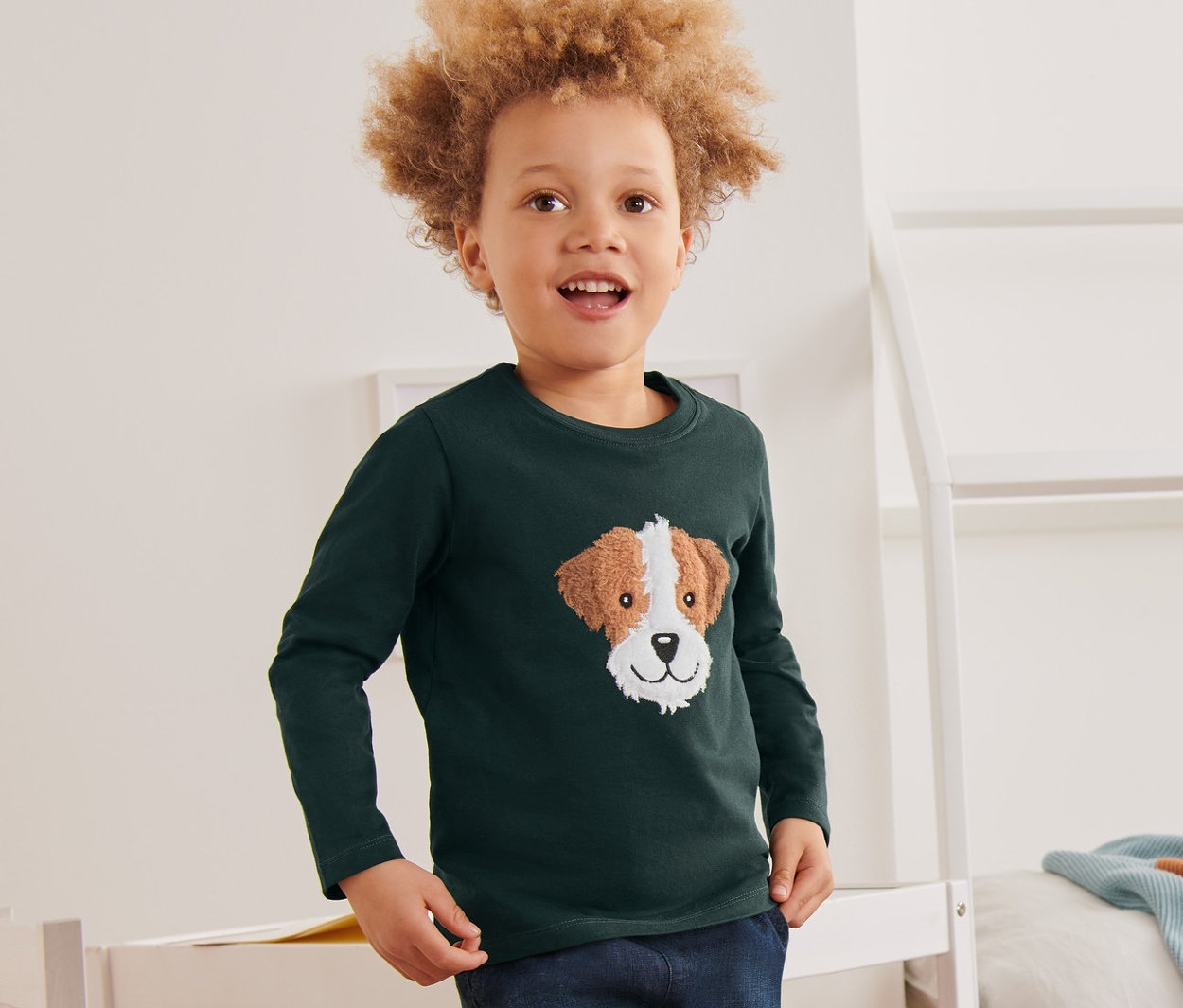 Junge trägt ein Kleinkinder-Langarmshirt im Kinderzimmer.