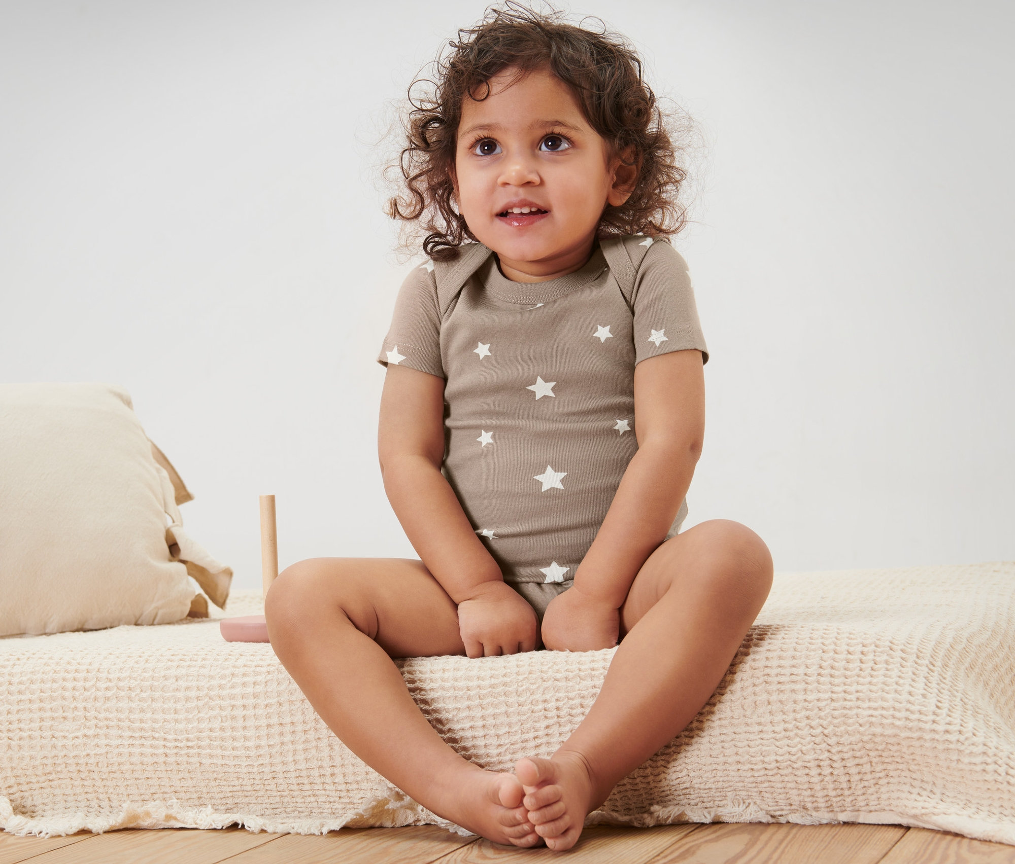 Kind sitzt auf einem Bett und trägt ein 5 Kurzarmbodys.