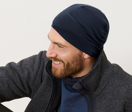 Mann sitzt auf Holzboden und trägt eine Mütze mit Wolle.