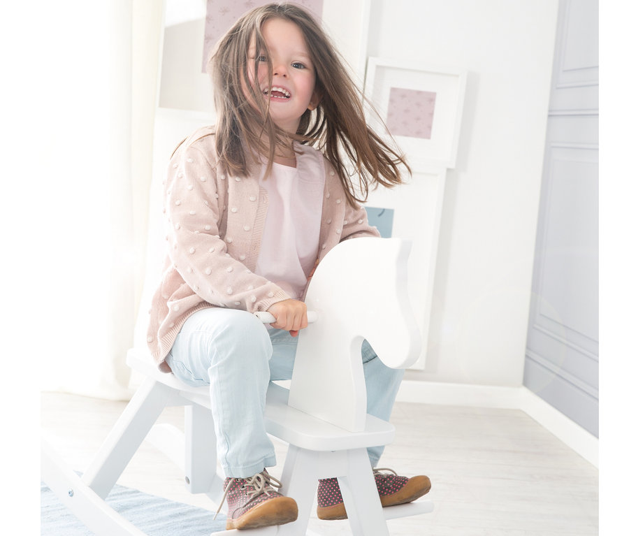 Ein Mädchen lacht und spielt auf einem weißen roba Schaukelpferd.