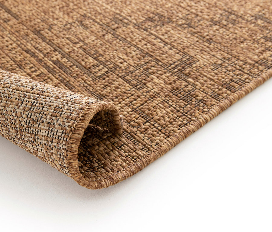 Detailaufnahme eines braunen Teppichs »Roy«, der auf einem weißen Hintergrund aufgerollt ist.