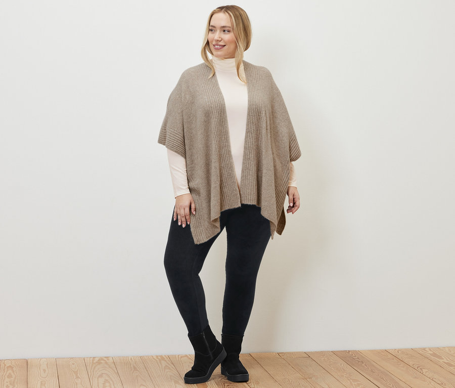 Frau trägt ein Strick-Cape, Cord-Leggings und ein cremeweißes Rollkragenshirt.