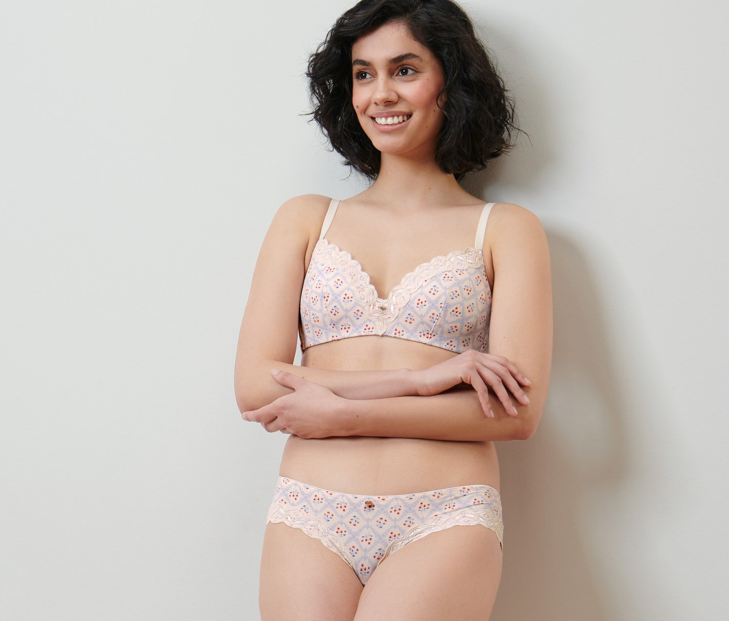 Lächelnde Frau posiert in Creme Unterwäsche Set mit Alloverprint und Spitze. Sie trägt 2 Brazil-Slips.