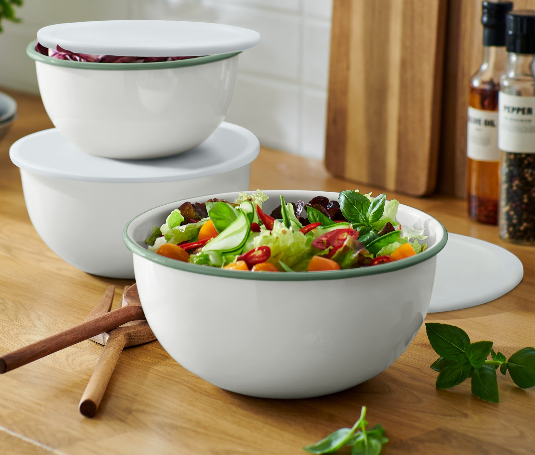 Drei Emaille-Servier-und-Zubereitungsschüsseln mit Deckeln stehen auf einer Küchentheke, die grösste Schüssel ist mit Salat gefüllt.