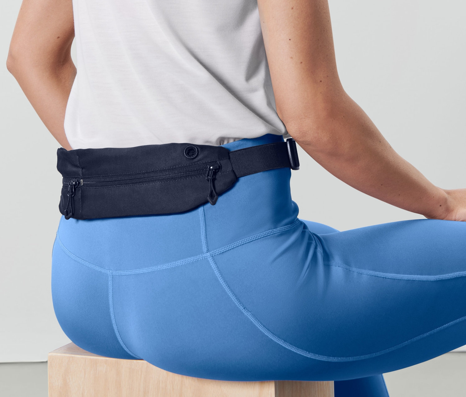 Frau sitzt und trägt blaue Leggings und einen Sportgürtel.