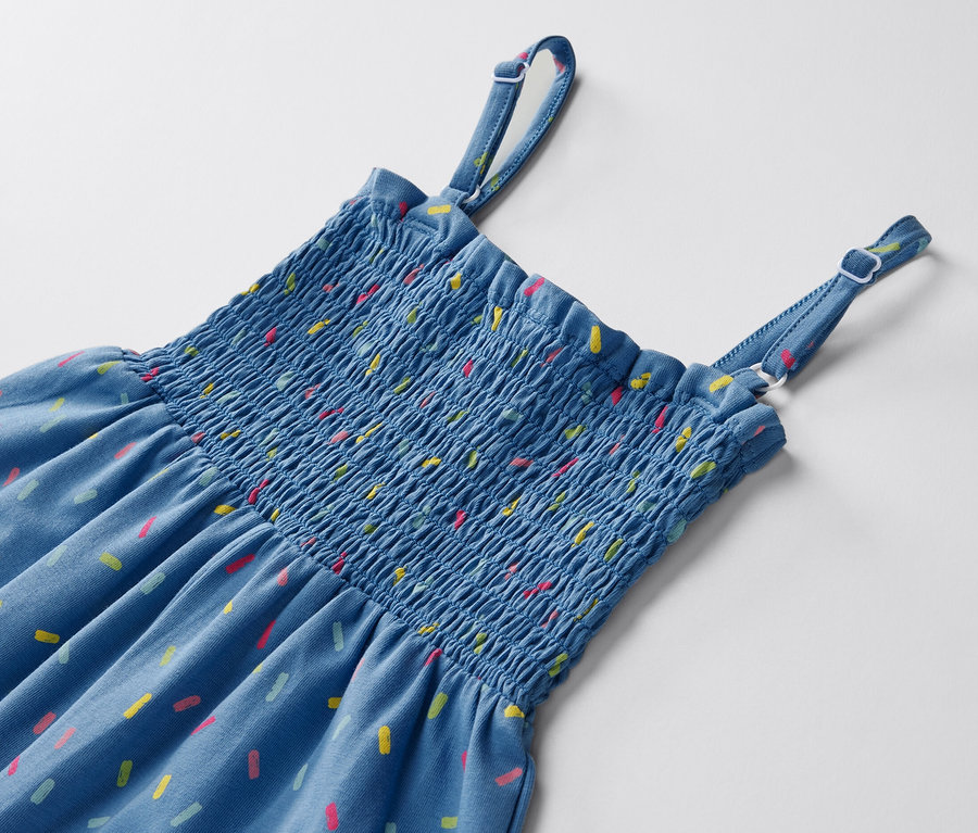 Detailansicht eines blauen Jumpsuits in 7/8-Länge mit bunten Mustern auf weißem Hintergrund.