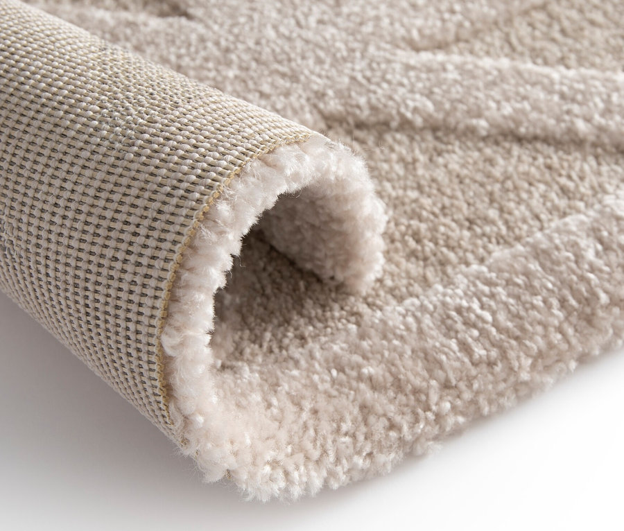 Detailaufnahme eines beigen Teppichs »Cosmo« Geo, teilweise aufgerollt, mit geometrischem Muster.