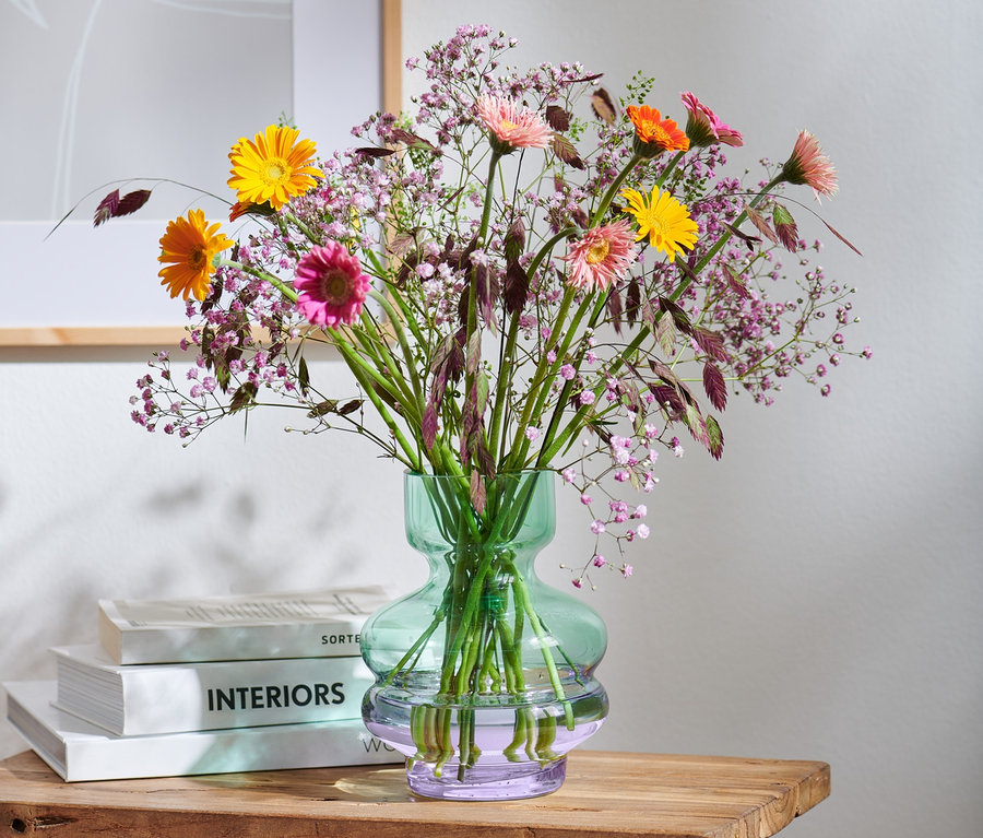 Blumen in einer Vase auf einem Holzhocker.