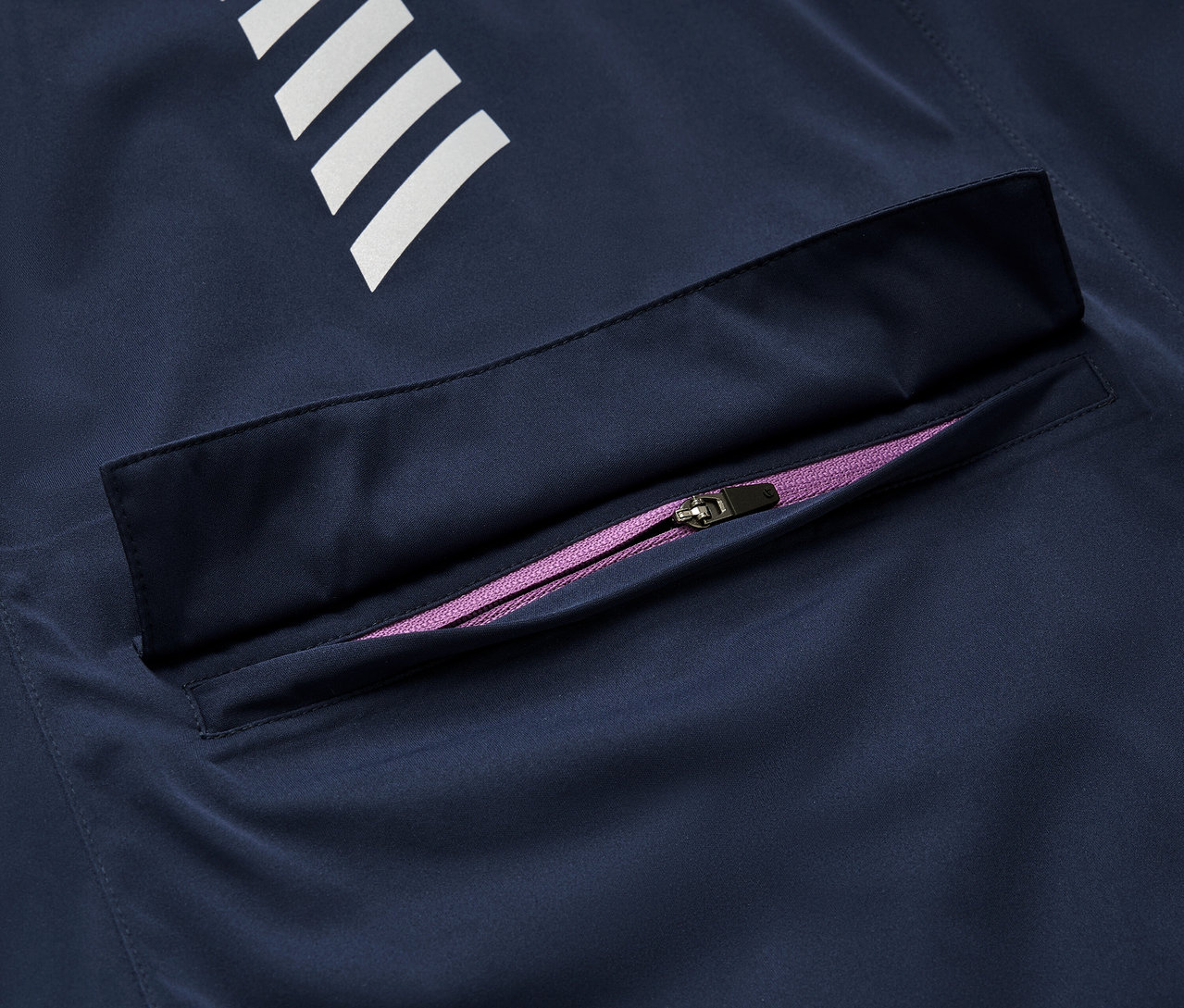 Detail einer dunkelblauen Rad-Regenjacke mit weißen Streifen und einem lila Reißverschluss.