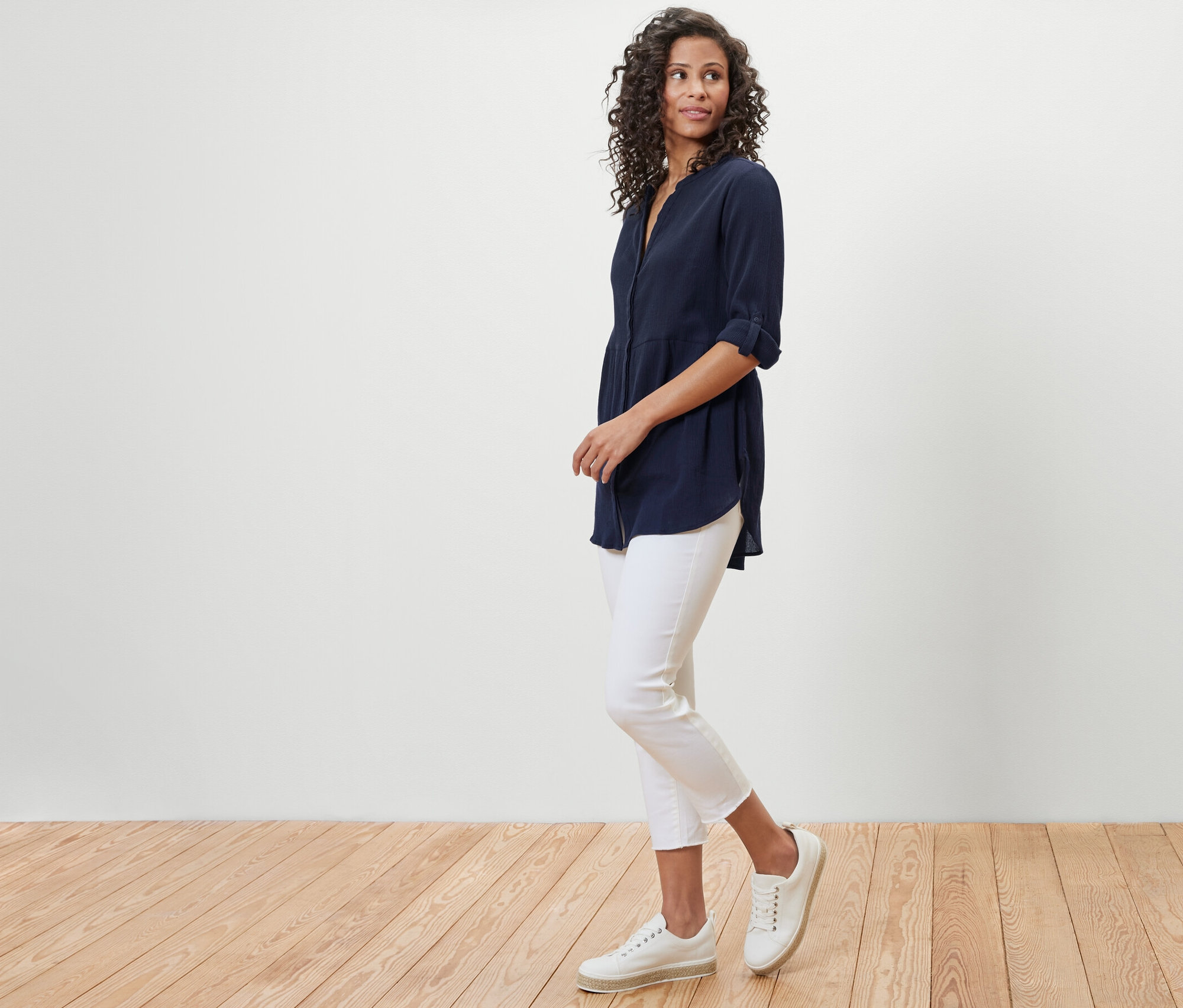 Frau in marineblauer Longbluse und weißen Hosen posiert auf Holzboden.