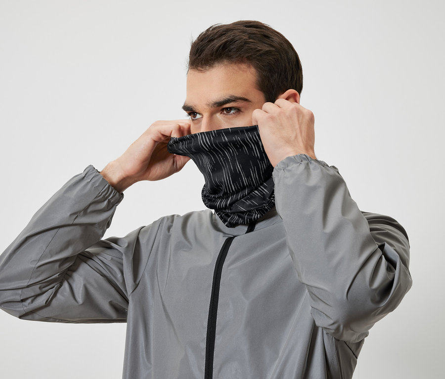 Mann zieht sich einen schwarzen Nackenwärmer mit weißen Streifen an und trägt eine graue Jacke.