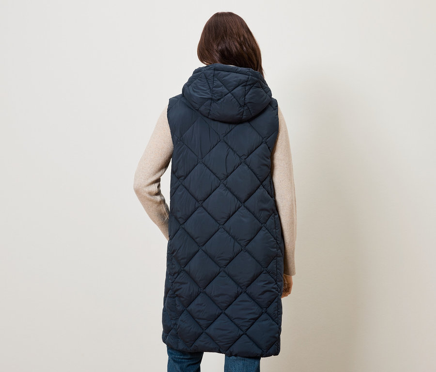 Frau von hinten trägt eine lange, gesteppte, dunkelblaue Weste mit Kapuze.