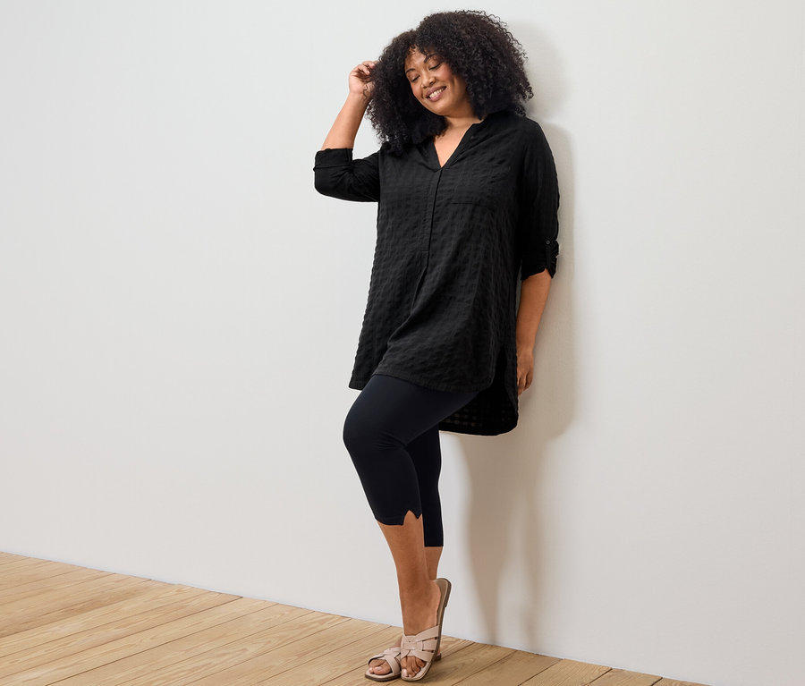 Frau posiert in schwarzer Longtunika mit Webstruktur und 3/4-Leggings mit Detail.