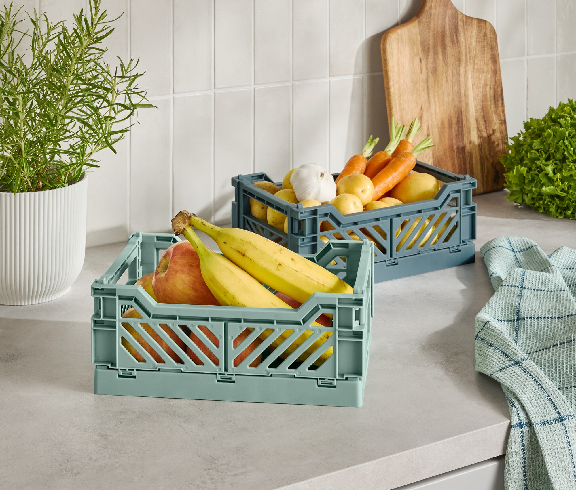 Zwei Kunststoffkörbe mit Obst und Gemüse auf einer Küchentheke.