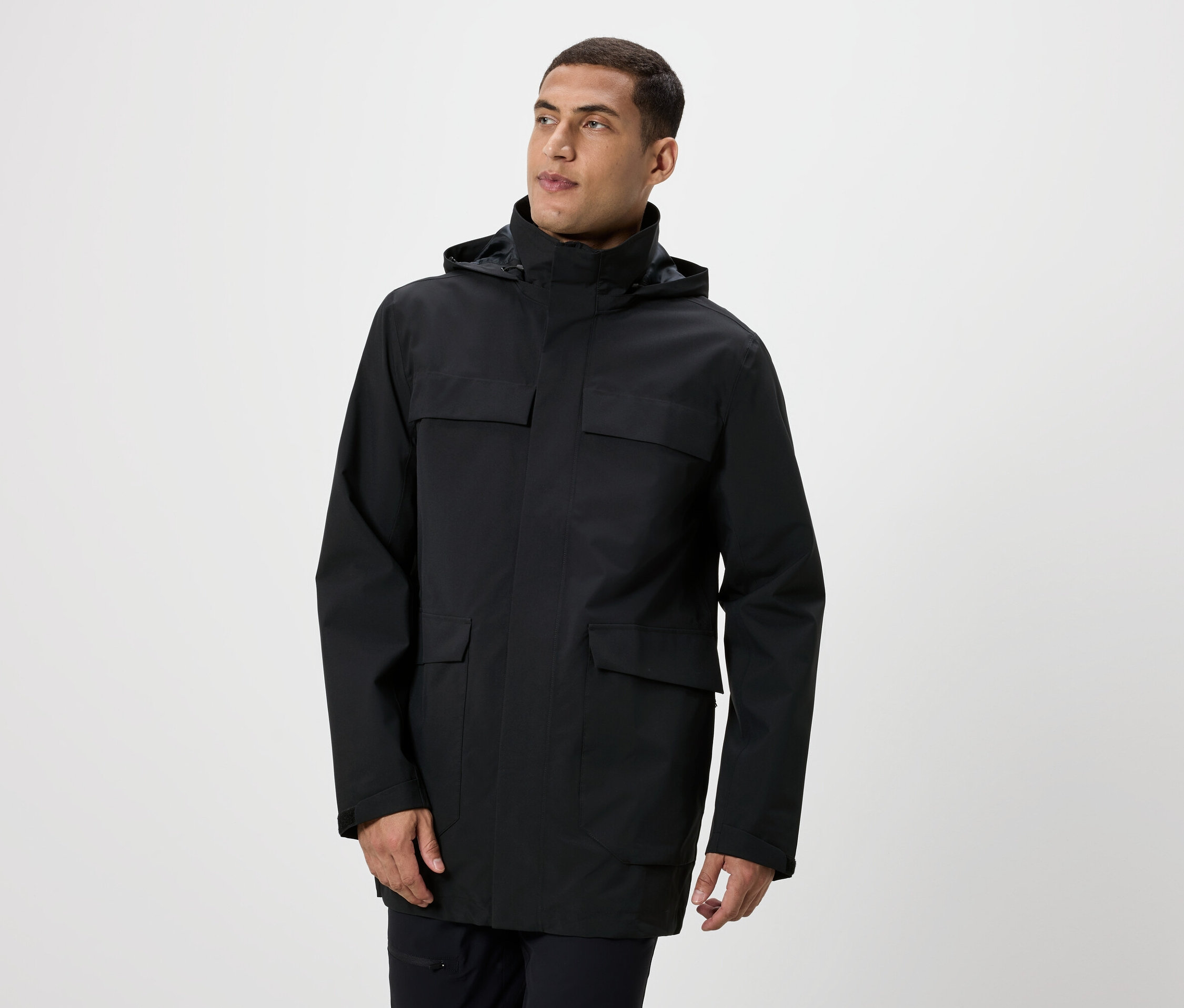 Mann posiert in einer schwarzen Jacke mit Kapuze und Taschen.