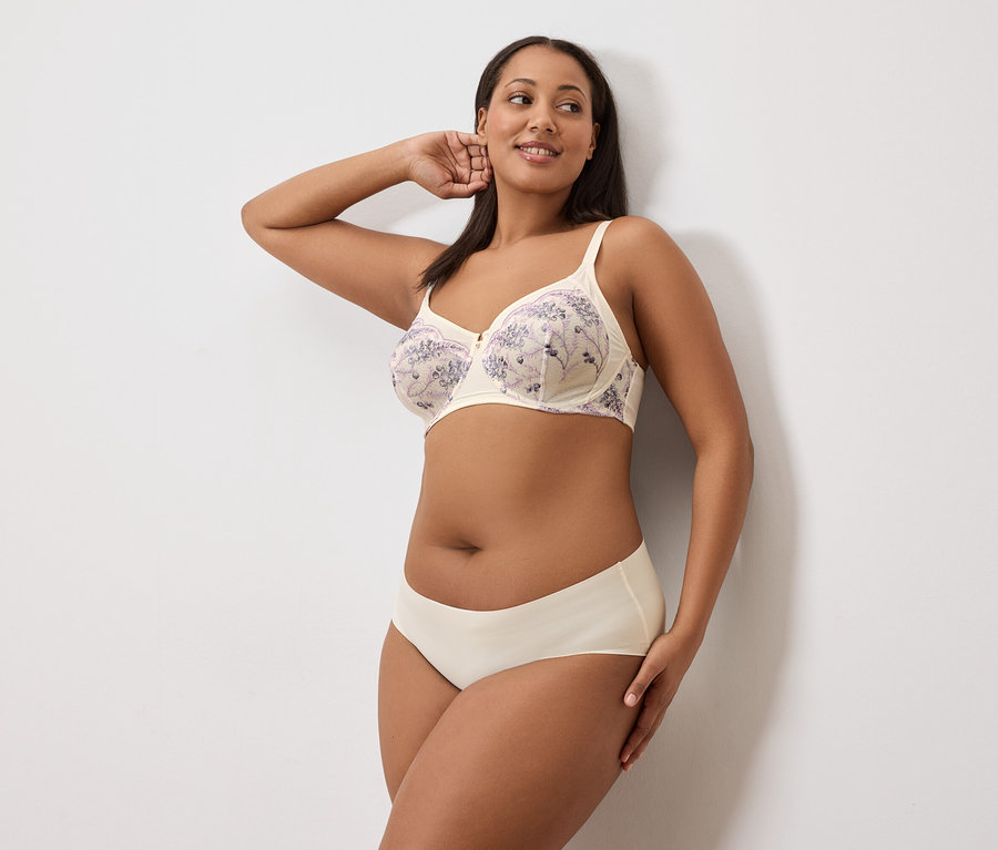 Frau posiert in BH und Unterhose vor weißem Hintergrund.