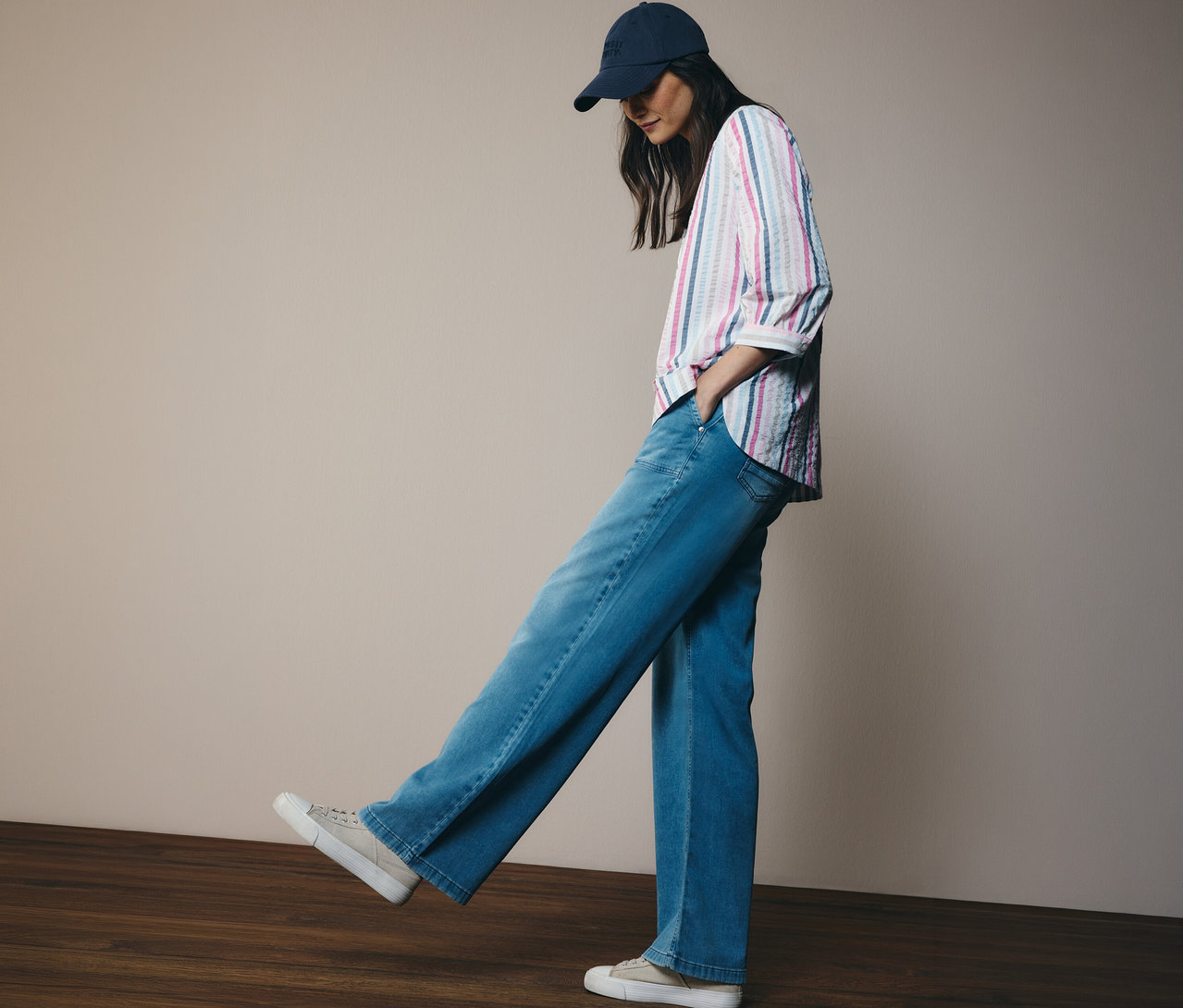 Frau mit Kappe, Jeans und CECIL Hemdbluse mit Streifen. Sie steht auf einem Holzfußboden.