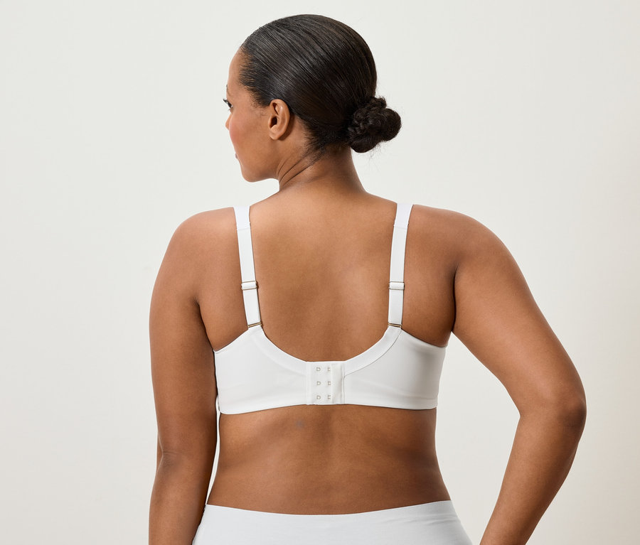 Rückansicht einer Frau mit Duttfrisur, die einen weißen BH und Unterwäsche trägt.