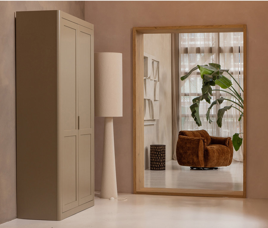 Beiger Kleiderschrank neben einer Stehlampe. Im Spiegelbild ist ein brauner Sessel und eine Pflanze zu sehen.