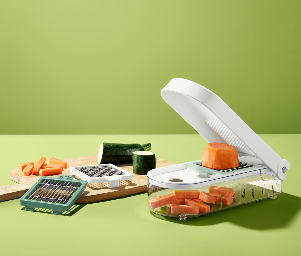 Obst- und Gemüseschneider mit geschnittener Karotte und Zucchini auf einem Schneidebrett.