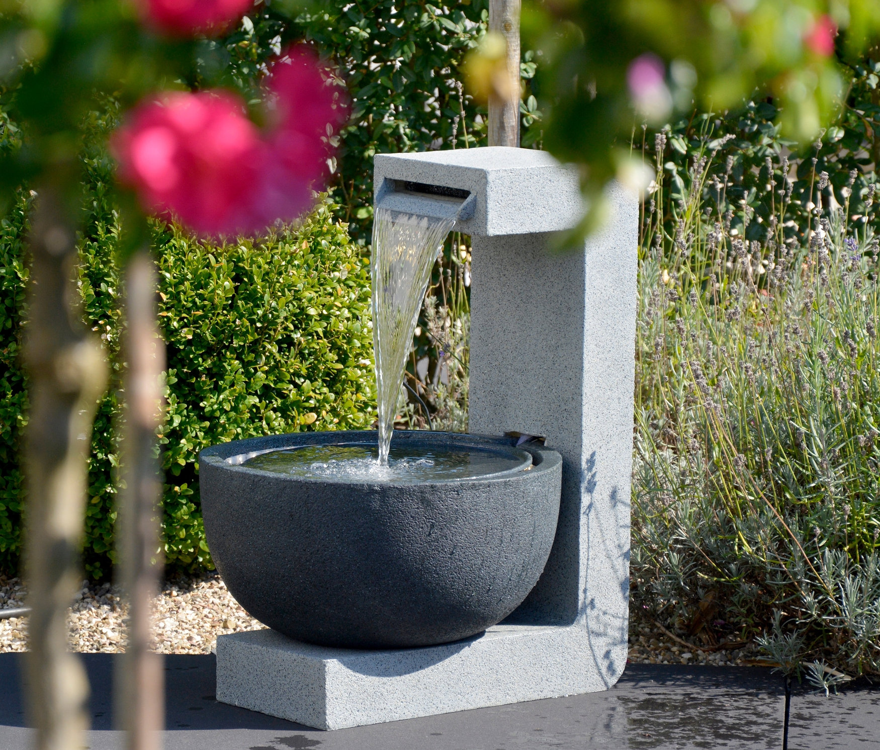 Wasser fließt in die Steinschale des Dobar Gartenbrunnens, im Hintergrund Grün.