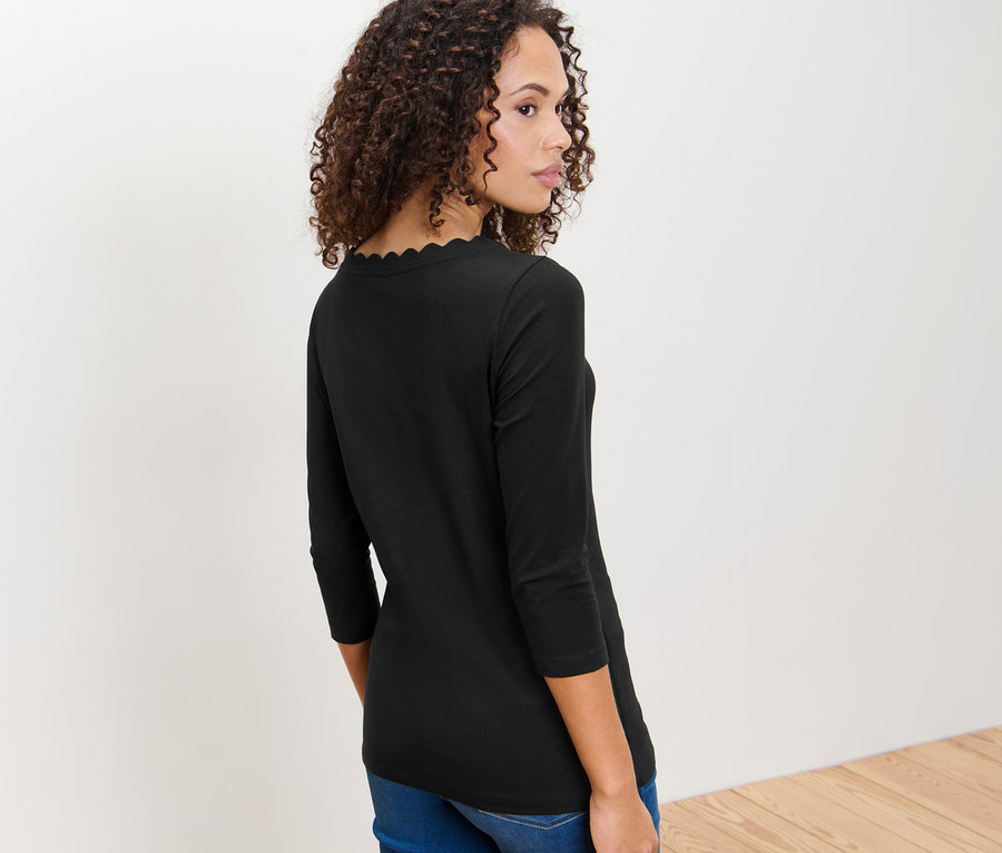 Frau mit braunen lockigen Haaren, die über ihre Schulter blickt und ein schwarzes Shirt mit 3/4-Arm trägt.