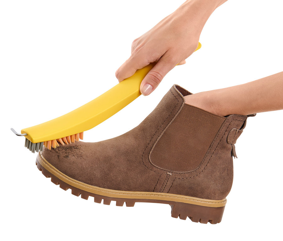 Eine Hand reinigt einen braunen Wildlederschuh mit einer 3-in-1-Schuhreinigungsbürste.